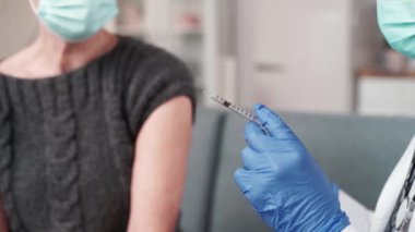 Koruyucu maskeli doktor hastasına aşı enjekte ediyor..