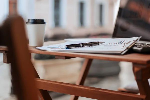 Nahaufnahme. Kaffee zum Mitnehmen und Finanzplan auf der Café-Terrasse. — Stockfoto