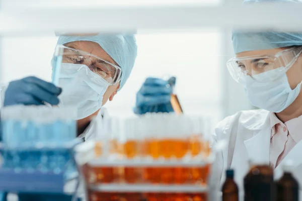 Cientistas em máscaras protetoras em pé na frente de um rack de tubos de ensaio . — Fotografia de Stock