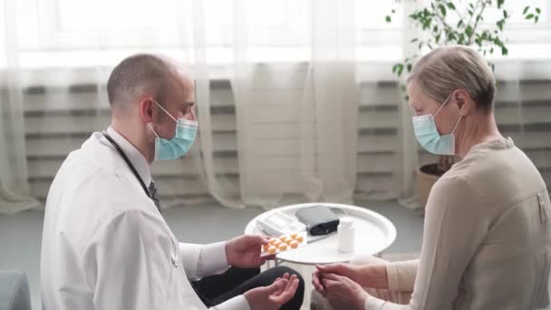 Médico está dando un paquete de pastillas y consultar a su paciente durante una visita a casa. — Vídeos de Stock