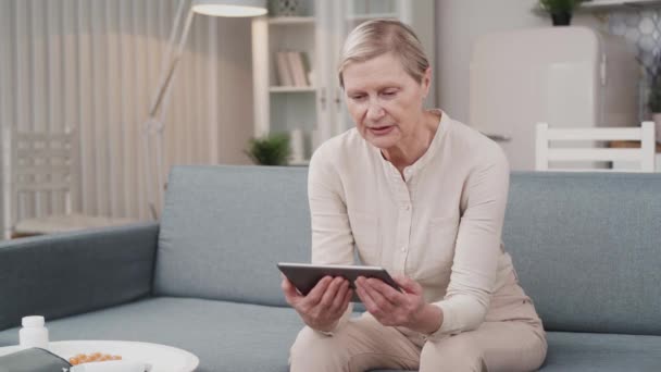 Anciana mayor sosteniendo una tableta digital llamando al médico en casa. — Vídeos de Stock