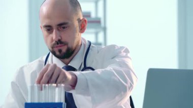 Araştırmacı laboratuvar tüpündeki sıvıya bakıyor ve testlerin sonuçlarını yazıyor..