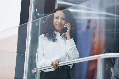 Asansöre binerken akıllı telefonuyla konuşan gülümseyen genç bir kadın..