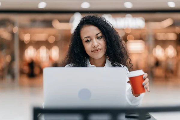 young woman with a takeaway coffee is working on her laptop.