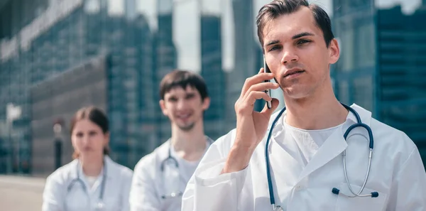 Bir hastane binasının yanında duran akıllı telefonlu bir doktor. . — Stok fotoğraf