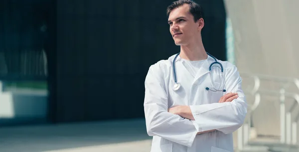 Tired young doctor standing near the entrance to the hospital . — Stock Photo, Image