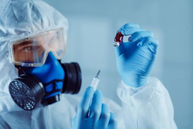 Yakın plan. Araştırmacının elinde bir şırınga ve test edilen aşının ampulü var..