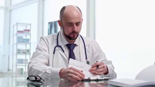 Doctor is making notes in the medical record during the visit of his patient . — Stok video