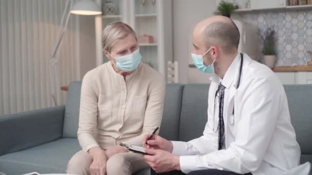 Doctor writing a prescription to his patient during a home visit. — Video Stock