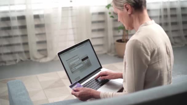 Mujer madura escribiendo un número de tarjeta bancaria en el teclado de su computadora portátil. — Vídeos de Stock