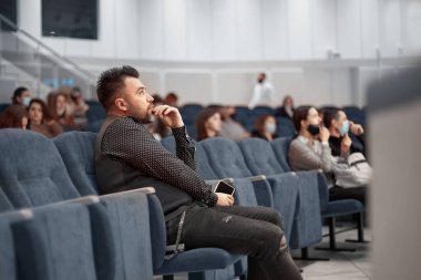 Akıllı telefonlu düşünceli bir adam konferans salonunda oturuyor..