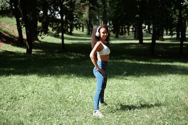 Mujer joven con auriculares hace gimnasia en el parque. —  Fotos de Stock