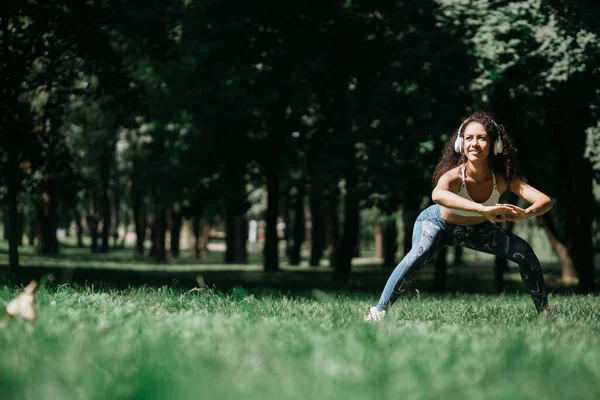 Usmívající se žena ve sluchátkách dělá protahování před jogging outd — Stock fotografie