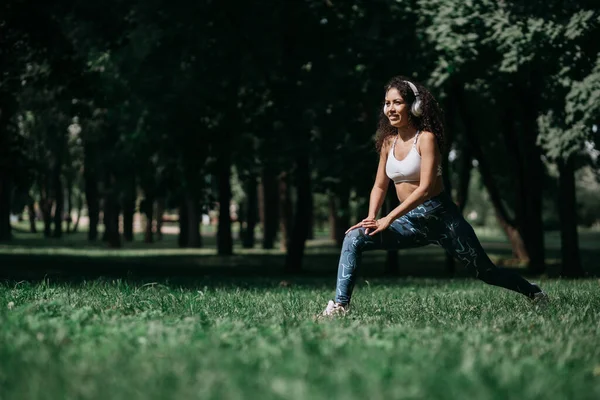 Smiling woman in headphones doing stretching before jogging outd — Stock Photo, Image