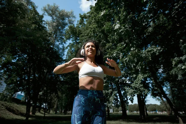 Glimlachende vrouw met koptelefoon uitvoeren van fitness-oefeningen in een — Stockfoto