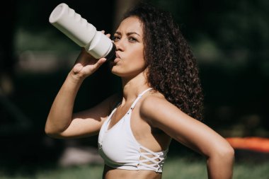 Sporcu genç kadın idmandan sonra su içiyor..