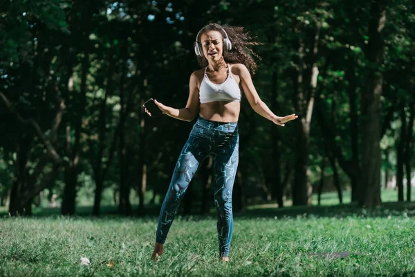 Sporty woman with a smartphone dancing in a city park . — Stock Photo, Image