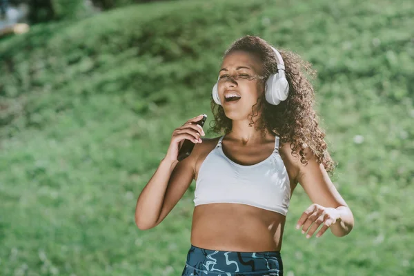 Sportovní žena s smartphonem tančící v městském parku . — Stock fotografie