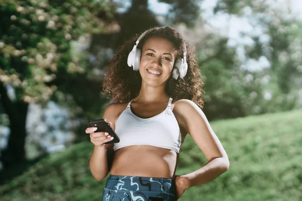 Sportovní žena ve sluchátkách pomocí smartphonu v parku . — Stock fotografie