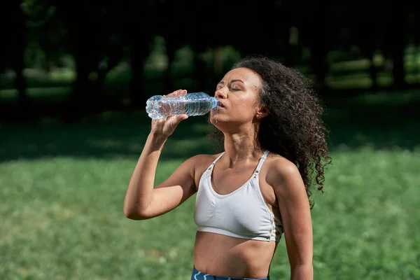 Vermoeide jonge vrouw drinkt water na een sporttraining. — Stockfoto