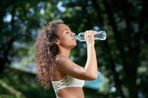 Vermoeide jonge vrouw drinkt water na een sporttraining. — Stockfoto