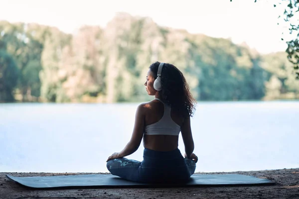 Mulher desportiva usando fones de ouvido meditando na posição de lótus — Fotografia de Stock