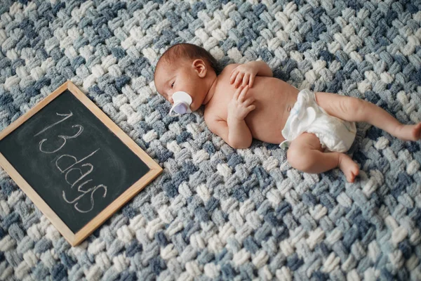 Pasgeboren baby met een fopspeen naast een schrijfbord . — Stockfoto