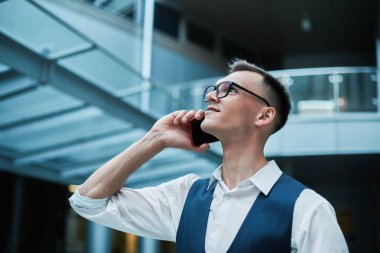 Lobb 'da elinde kahve ve akıllı telefonuyla bekleyen bir adam.