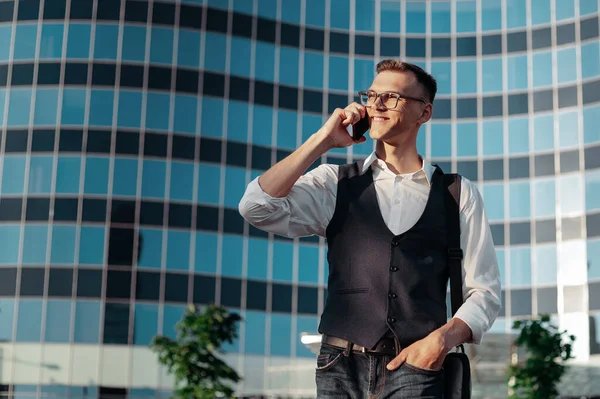 Glücklicher junger Mann, der vor einem Büro auf einem Smartphone spricht. — Stockfoto