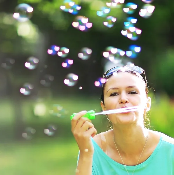 Gorgeous young brunette girl blowing soap bubbles in sunlit park. — Stock Photo, Image