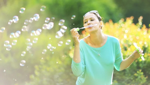 Nádherná mladá brunetka foukání mýdlové bubliny v slunný park. — Stock fotografie