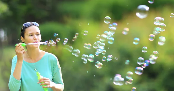 Nádherná mladá brunetka foukání mýdlové bubliny v slunný park. — Stock fotografie