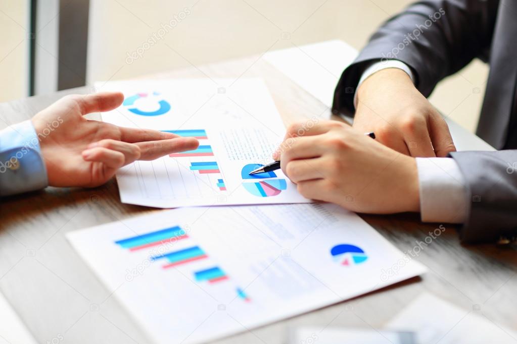 Image of human hands with pens pointing at business document at meeting