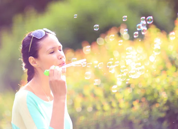 Hermosa chica morena joven soplando burbujas de jabón en el parque soleado . — Foto de Stock