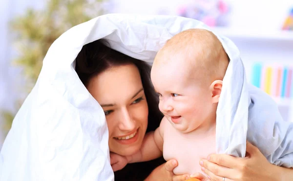 Mutlu bir aile. Anne ve bebek battaniyenin altında oynuyor ve gülümsüyor. — Stok fotoğraf