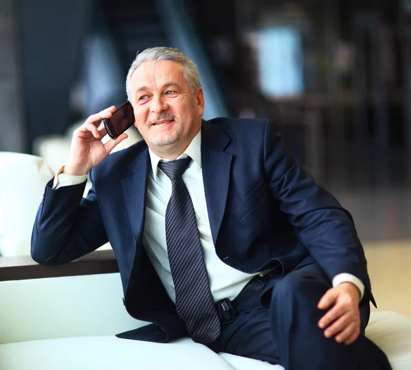 Hombre de negocios sonriente sentado y hablando por teléfono en la oficina —  Fotos de Stock