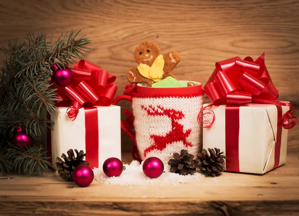 Taza de té o café. Dulces y especias. Decoraciones de Navidad. Fondo de madera. Un regalo con una cinta roja . — Foto de Stock