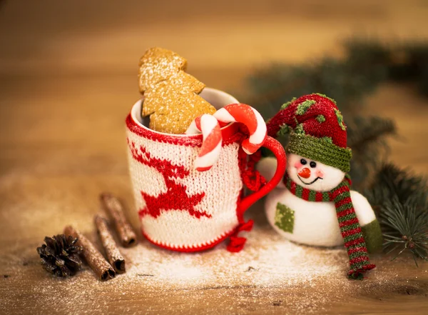 紅茶やコーヒーのマグカップです。スイーツとスパイス。雪だるまとクリスマスの装飾。木造背景. — ストック写真