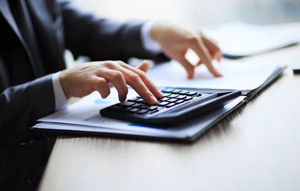 Business people counting on calculator sitting at the table. Close up of hands and stationery — Stock Photo, Image