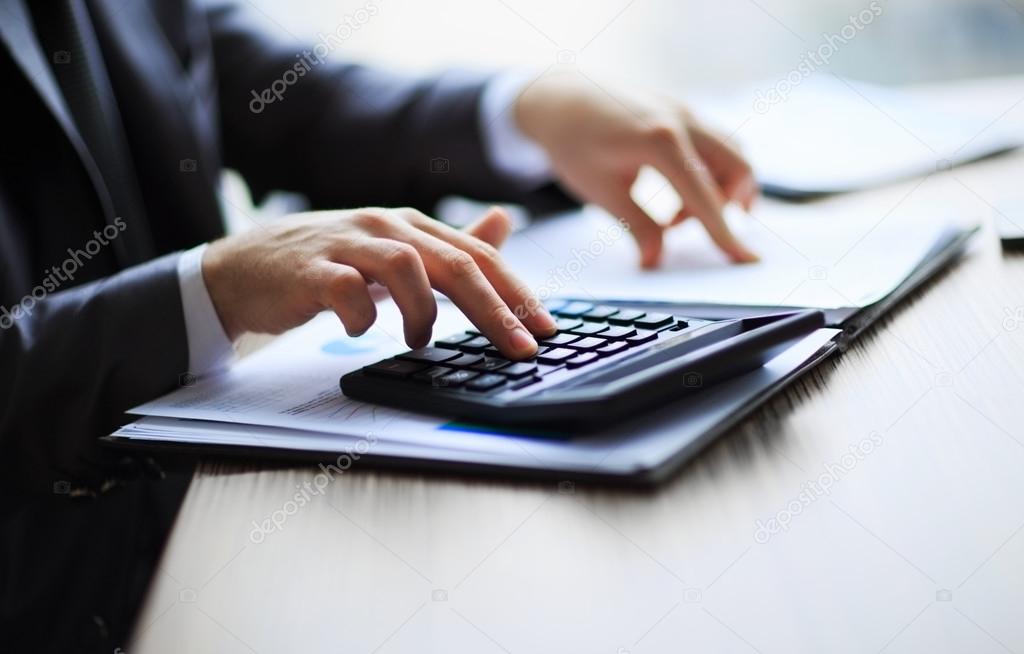 Business people counting on calculator sitting at the table. Close up of hands and stationery