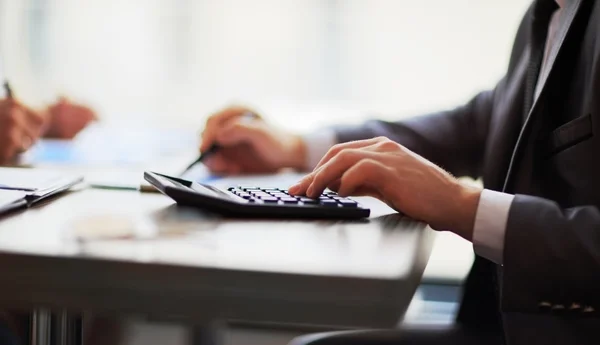 Les gens d'affaires comptent sur la calculatrice assise à la table. Gros plan sur les mains et la papeterie — Photo