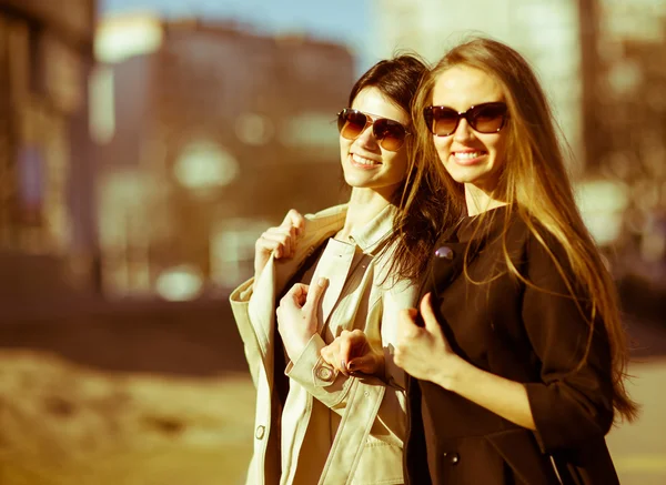 Dos hermosas chicas felices en gafas de sol en el fondo urbano. Jóvenes activos. Al aire libre — Foto de Stock