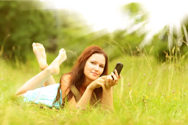 Životní styl, letní dovolená, technologie, volný čas a lidé koncept - usmívající se dívka s smartphone ležet na trávě v parku — Stock fotografie