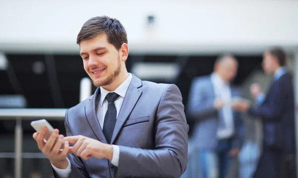 Usinessman debout à l'intérieur d'un immeuble de bureaux moderne regardant sur un téléphone mobile — Photo