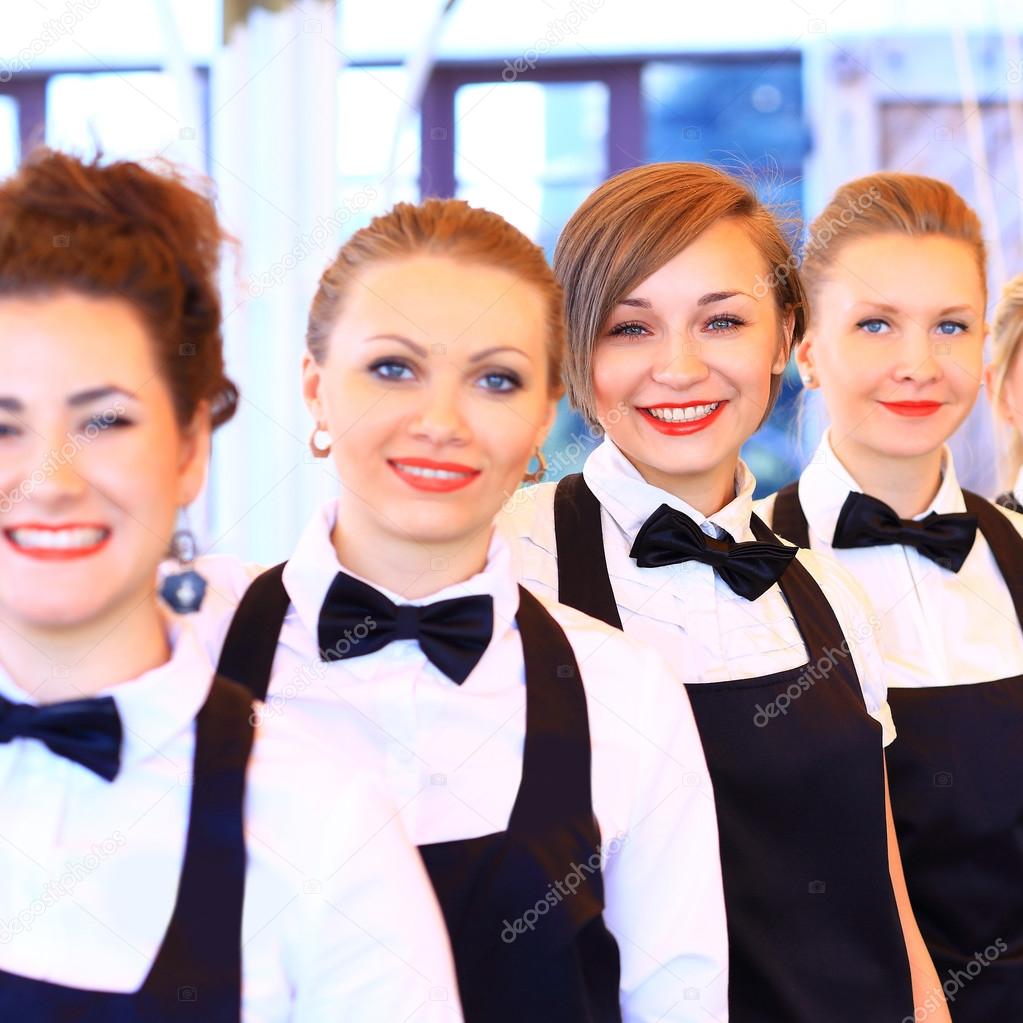 Large group of waiters and waitresses standing in row.