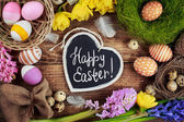 Černá deska s textem - Veselé Velikonoce. Barevné velikonoční vajíčka a květiny
