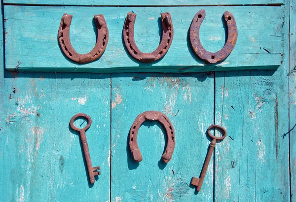 2 つのキーと木製のドアに掛かっている 4 つの蹄鉄 — ストック写真