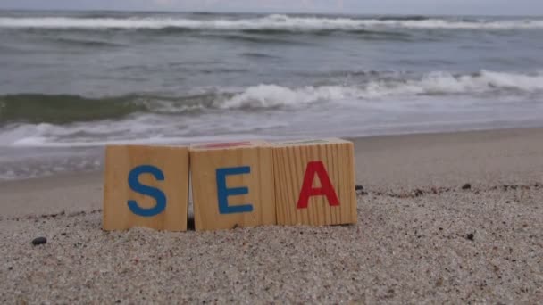 Слово SEA на деревянных кубиках на пляже в песке — стоковое видео