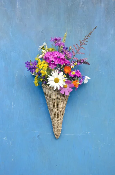 Wicker basket with summer flowers on blue wall — Stock Photo, Image