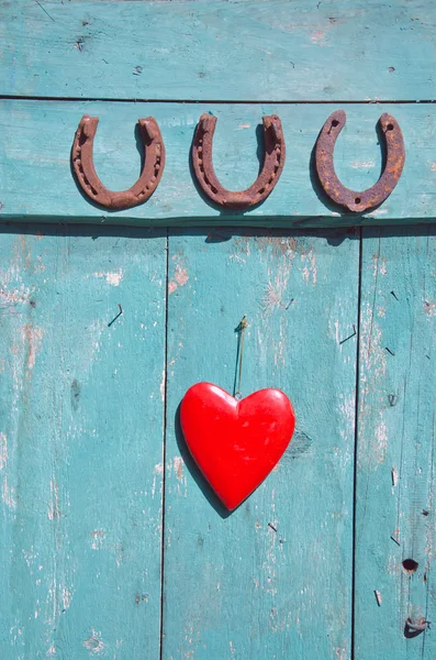 Drie roestig hoefijzer geluk symbool en rood hart op deur — Stockfoto